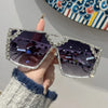 A hand holds a pair of geometric rhinestone fashion sunglasses against a colorful patterned background.