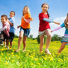 Tres niños sonrientes con mangas protectoras UV, de pie en un campo amarillo de flores bajo un cielo azul.