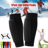 A pair of black ski shin pads are shown against a snowy mountain backdrop with skiers.