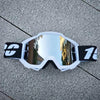 Une paire de lunettes de moto tout-terrain blanches avec des accents noirs posées sur une surface grise texturée.
