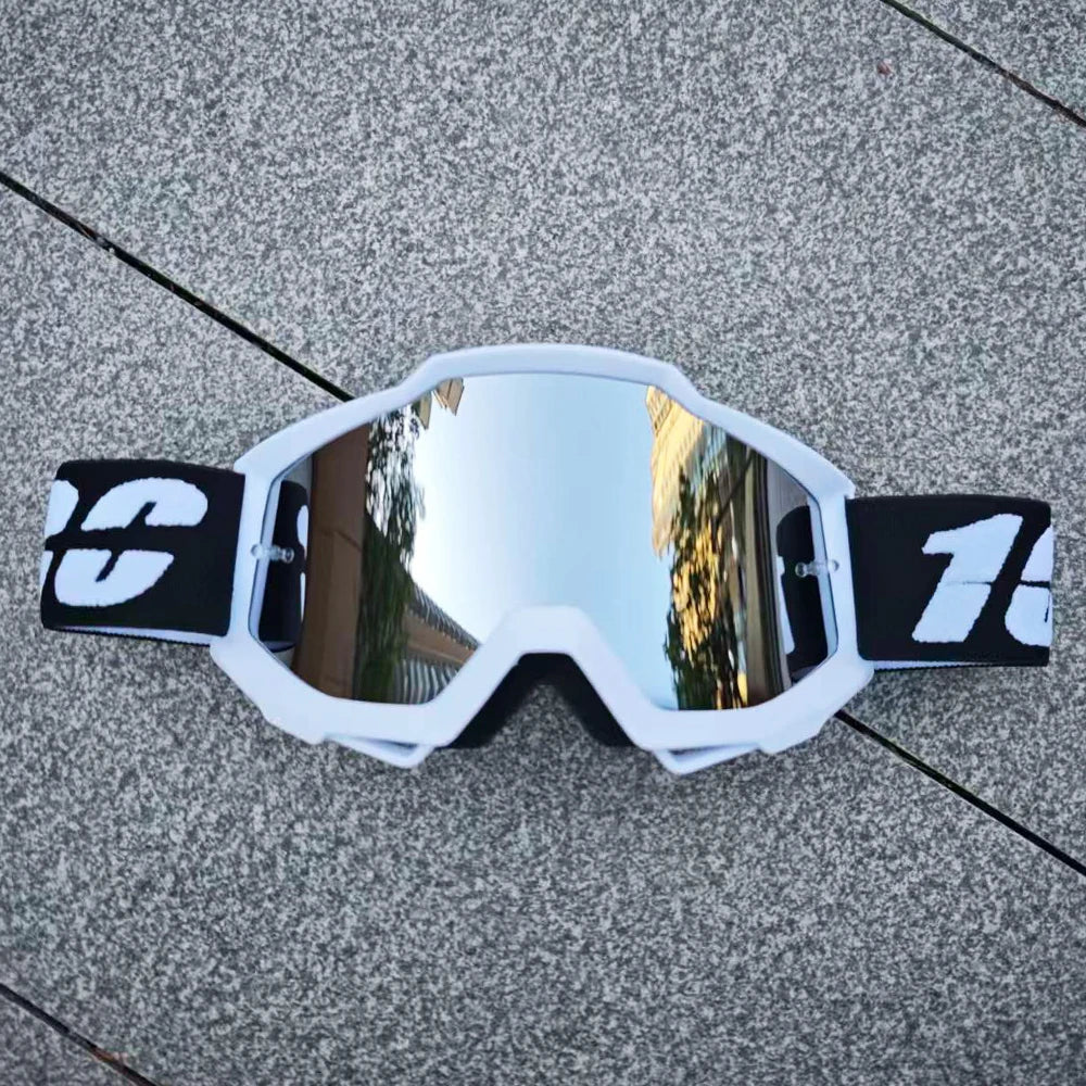 Une paire de lunettes de moto tout-terrain blanches avec des accents noirs posées sur une surface grise texturée.