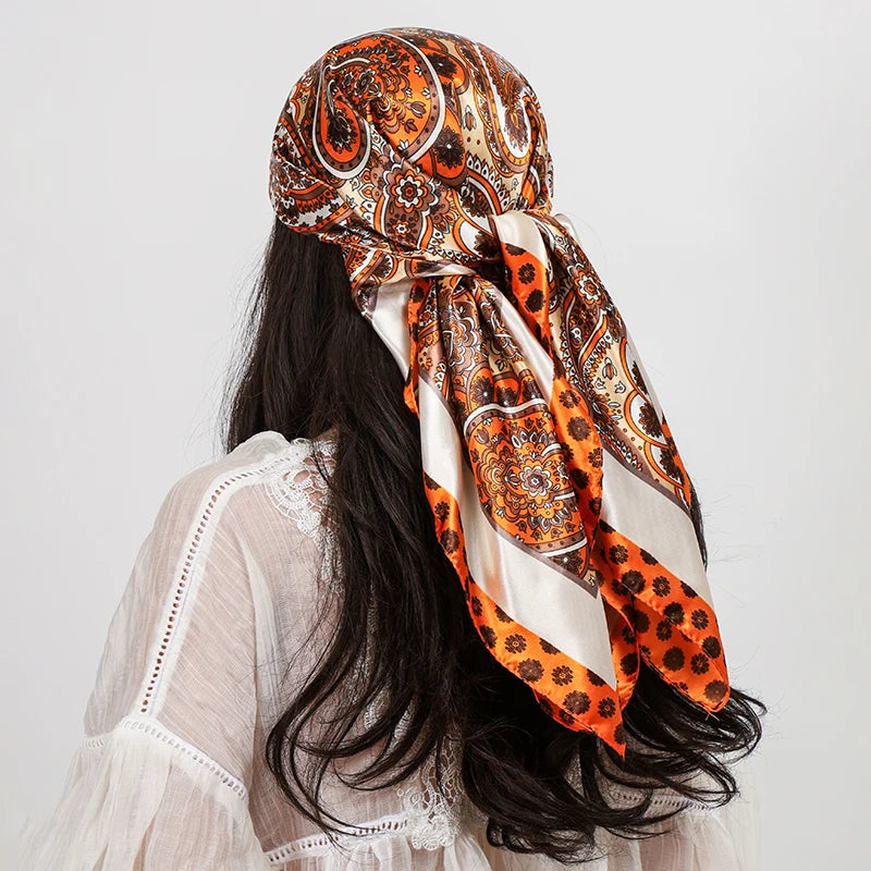A woman with long dark hair is wearing an orange and brown paisley silk shawl scarf draped around her neck.