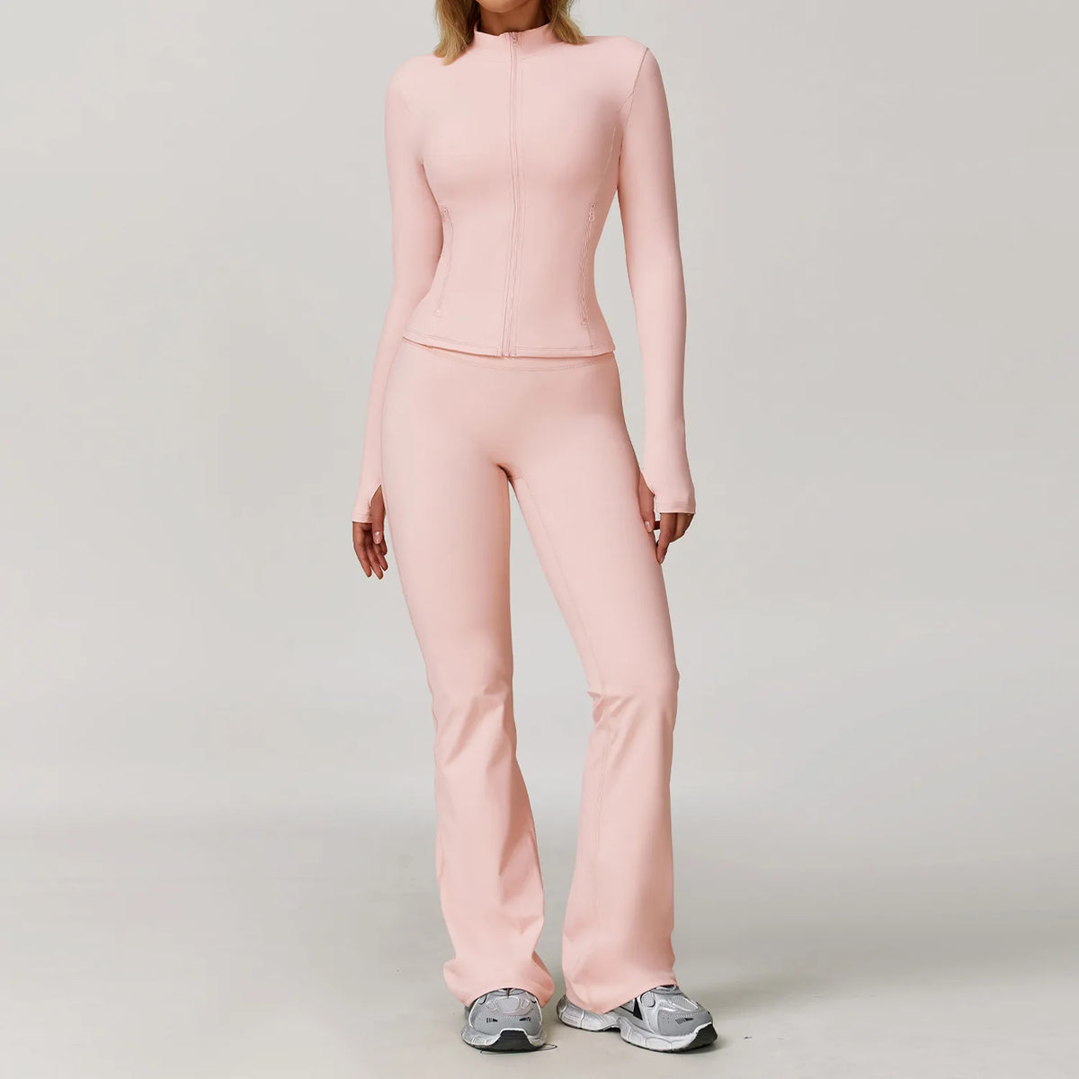 A woman wearing a light pink, long-sleeved yoga sports set consisting of a top and pants.