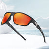 A pair of black sports sunglasses with bright orange lenses resting on a white surface against a blue sea background.