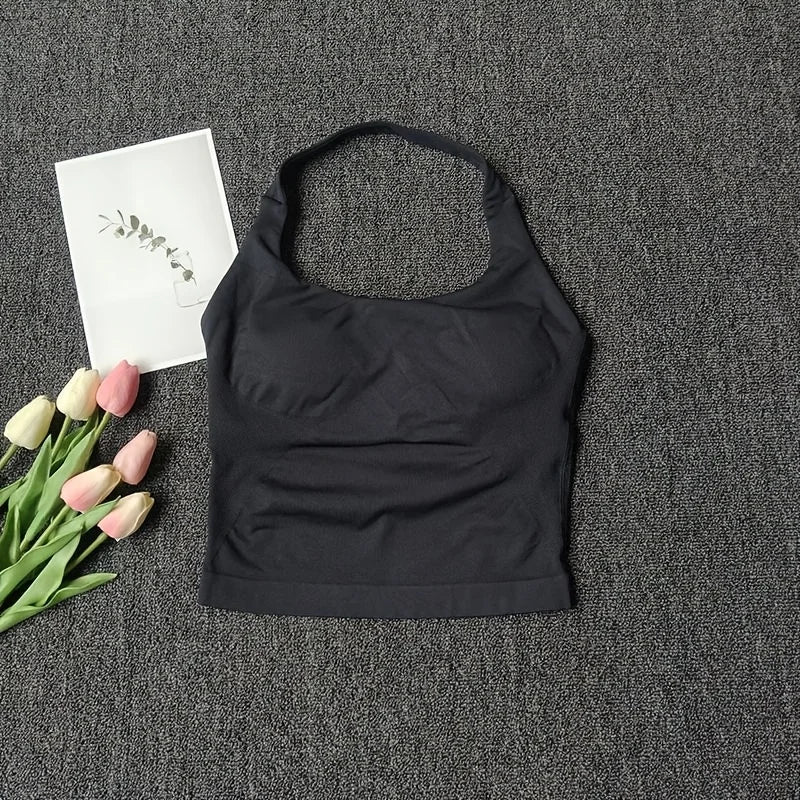 Black seamless sports camisole top laid on a dark gray textured surface with a white card and pink tulips.
