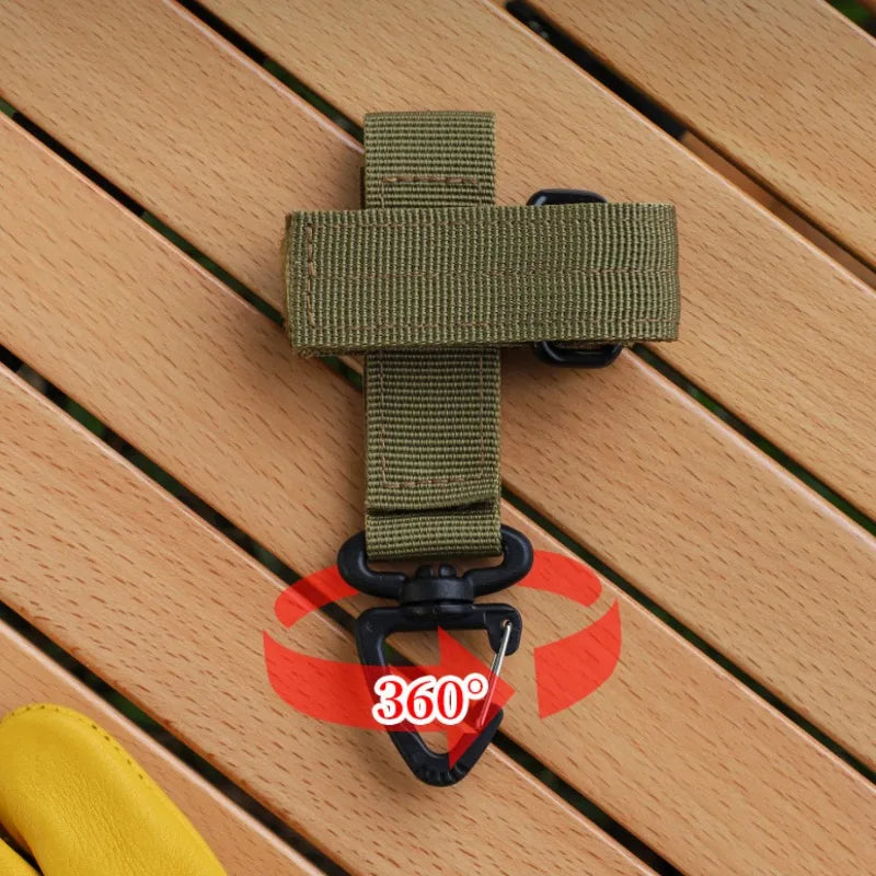 Tactical nylon glove hook with a green strap and black clip resting on a wooden surface.