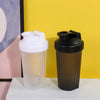 A clear and black leakproof protein shaker bottle standing on a white surface against a yellow background.