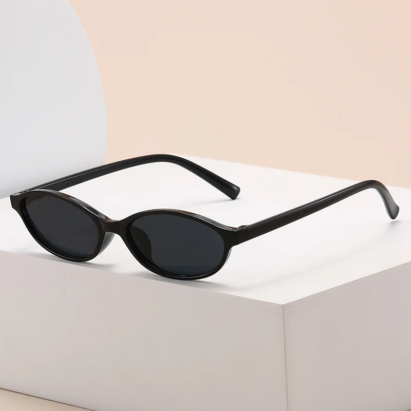 Black retro oval frame sunglasses resting on a white box.