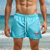 A muscular man wearing light blue quick-drying swim shorts on a beach.