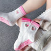 Chaussettes de yoga blanches avec broderie rose et adhérence anti-dérapante portées sur un pied.