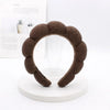 A brown sponge terry cloth headband for hair styling displayed on a white circular stand.