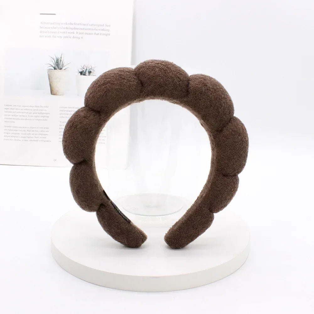A brown sponge terry cloth headband for hair styling displayed on a white circular stand.