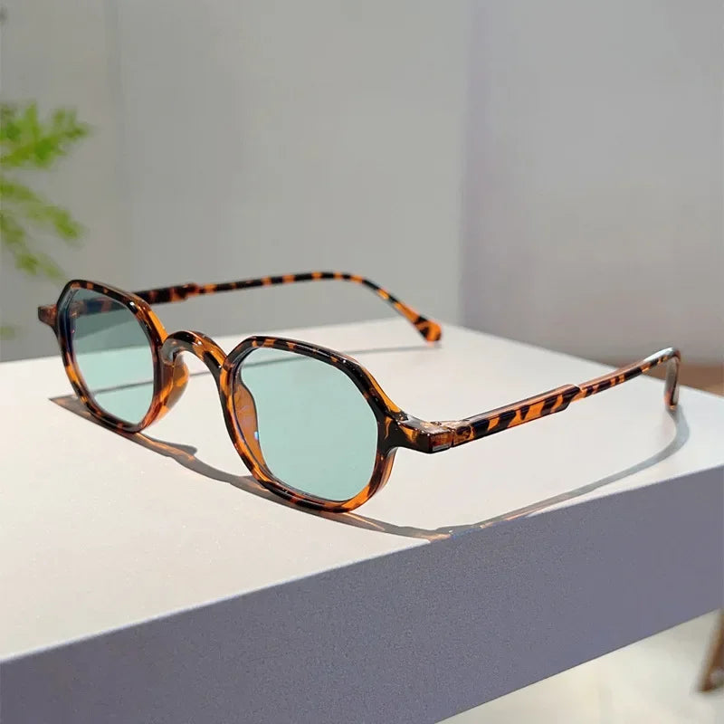 Vintage oval sunglasses with brown and black leopard print frames and light blue lenses resting on a white surface.
