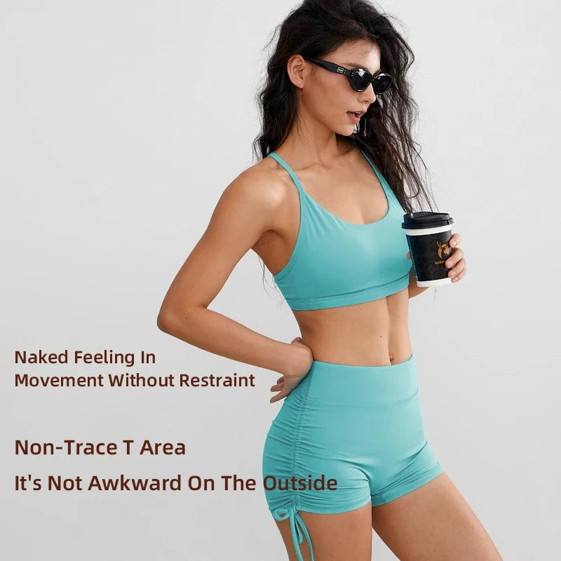 A woman models performance yoga shorts in teal fabric against a light gray background.