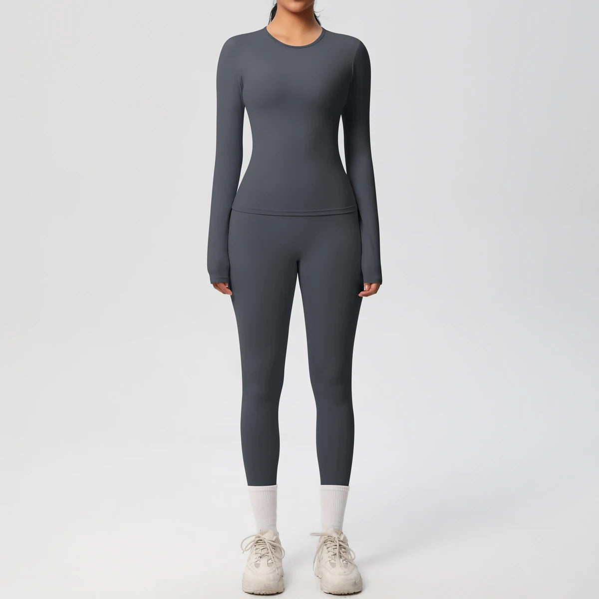 A woman wearing a full-length, long-sleeved charcoal gray performance yoga and gym set with white socks and light gray athlet