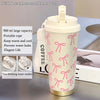 A pink insulated stainless steel travel mug with a lid and carrying strap is shown on a gray surface.
