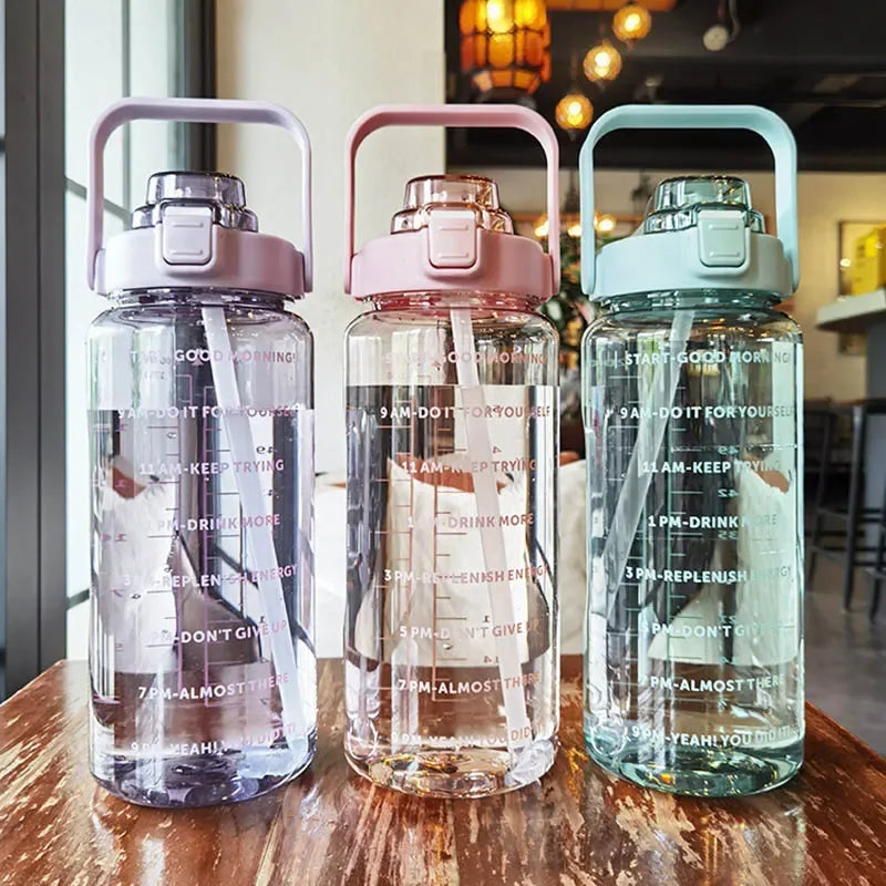Tres botellas de agua de vidrio transparente con tapas y pajitas rosas y verde azulado sobre una superficie de madera.