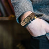 A close-up of a wrist wearing a brown paracord bracelet with a bronze American flag charm.
