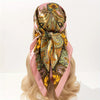 A pink satin square scarf with an ornate gold and green paisley pattern tied around a blonde hairstyle.