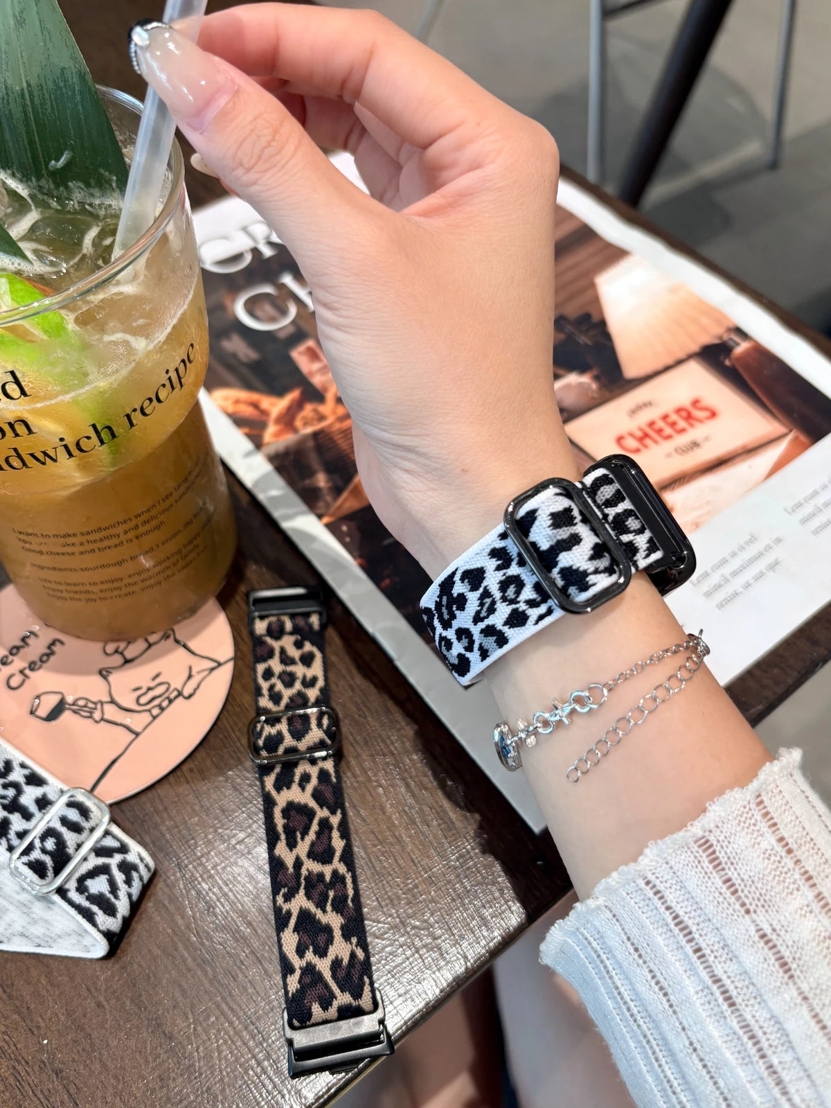 A hand wearing a leopard print silicone watch band is holding a glass of iced tea next to a menu.