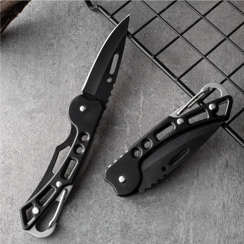 A black folding stainless steel survival knife is shown lying on a gray textured surface.
