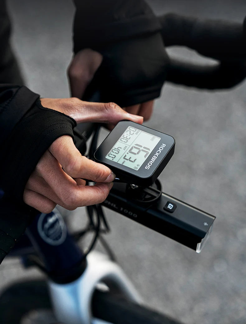 A hand is adjusting a black GPS cycling computer and speedometer mounted on a bicycle handlebar.