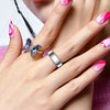 A close-up of a hand wearing a silver ring and a blue gemstone ring, with manicured nails.