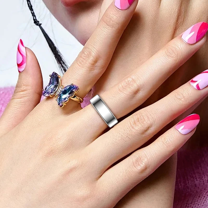 A close-up of a hand wearing a silver ring and a blue gemstone ring, with manicured nails.