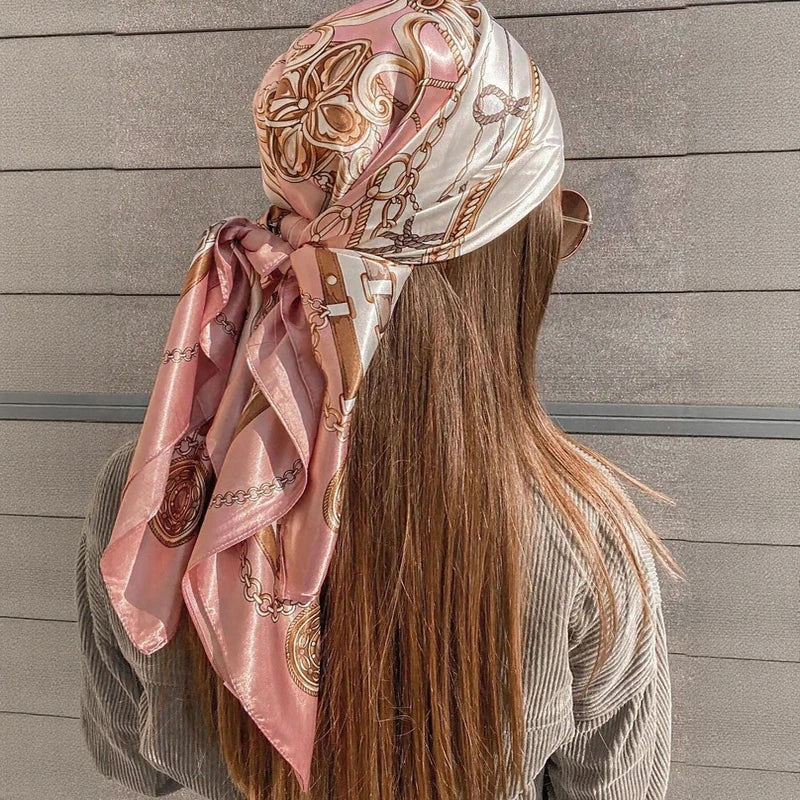 A woman shows the back of an elegant pink and cream satin square scarf tied in a flowing fabric.