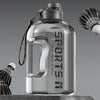 Klare, große wiederverwendbare Sportflasche mit Metallverschluss und Leine, auf grauer Oberfläche.