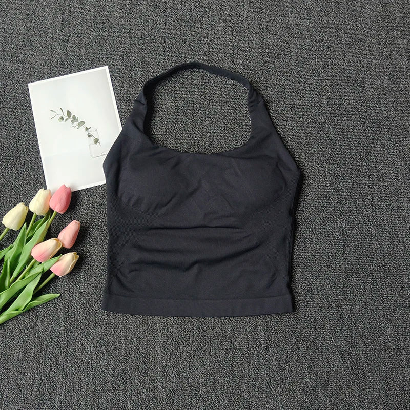 Black seamless yoga and pilates sports bra laid on a dark gray textured surface with pink tulips and a white card.