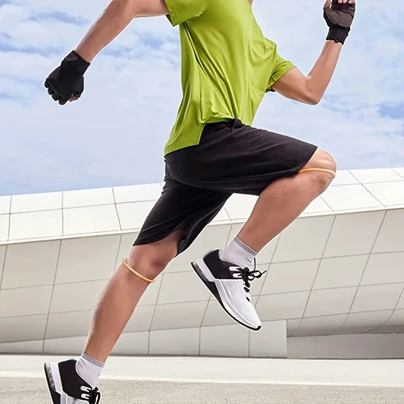 A person wearing a green shirt and black shorts is performing an athletic movement while using a knee brace strap.