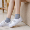 A pair of white canvas shoes with grey socks are shown resting on a light-colored floor next to a woven mat.