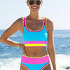 A woman wearing a color-block zigzag three-piece swimsuit set stands near the ocean.