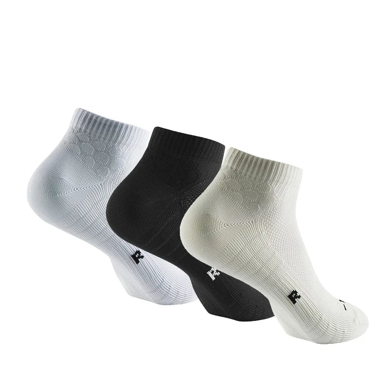 A set of three performance ankle socks in white, black, and off-white are displayed lying flat.
