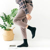 Une personne portant un pantalon marron et une chemise à carreaux, montrant des chaussettes noires à col roulé.