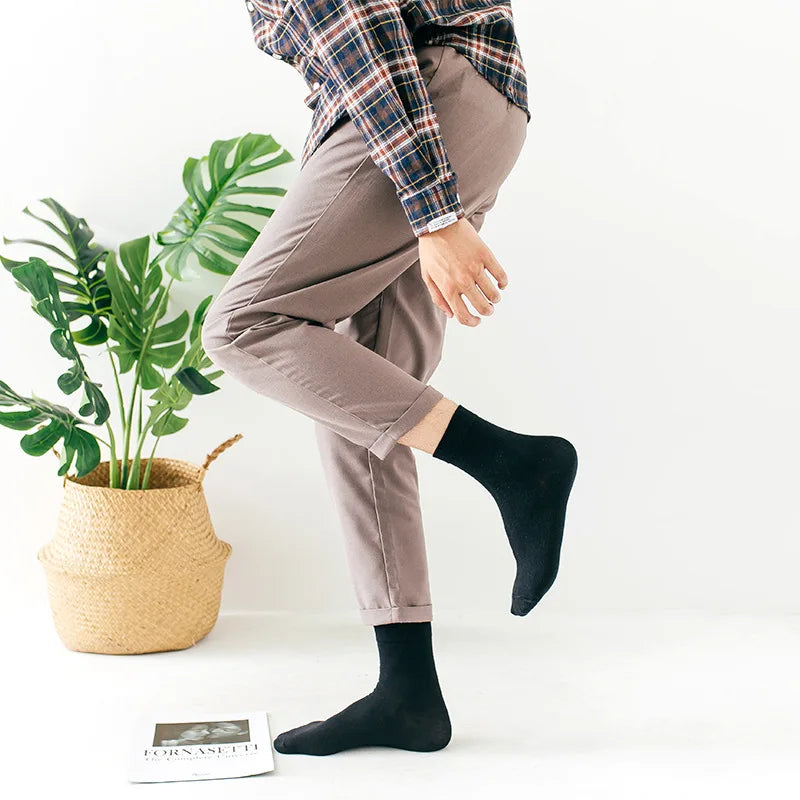 Une personne portant un pantalon marron et une chemise à carreaux, montrant des chaussettes noires à col roulé.