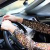A person's hands are gripping the steering wheel of a car while wearing patterned sun shading tattoo arm sleeves.