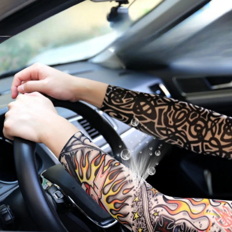 A person's hands are gripping the steering wheel of a car while wearing patterned sun shading tattoo arm sleeves.