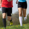 A person wearing black athletic shorts and compression socks is running outdoors.