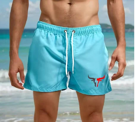 Light blue quick-drying men's swim shorts worn by a muscular man near the ocean.
