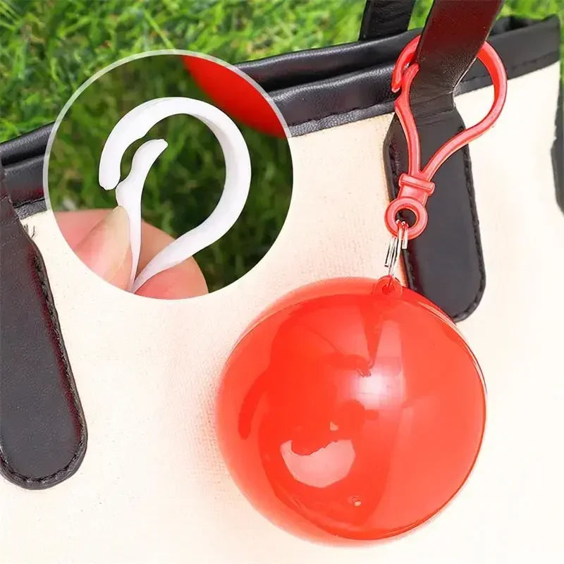 A bright red spherical rain poncho with a white handle is shown against a beige fabric background.