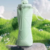 Botella de agua de silicona verde claro y plegable, apoyada sobre una roca con césped y vegetación frondosa.