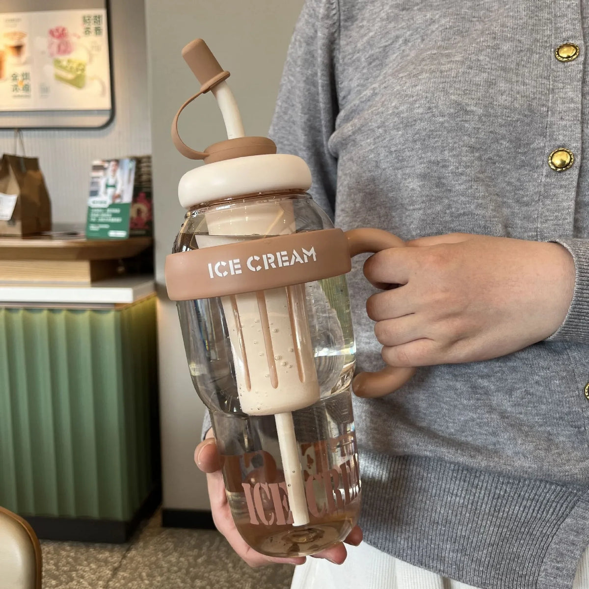 A hand holds a large capacity portable plastic drinking cup filled with ice cream and a straw.