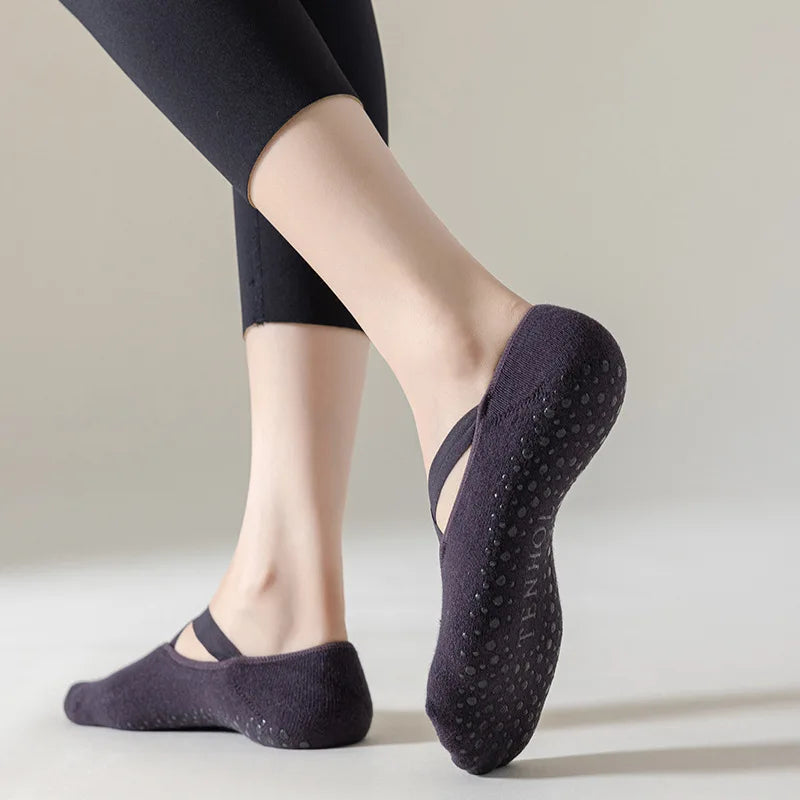 Una persona vistiendo calcetines de yoga y pilates ajustados de color gris oscuro, de pie contra un fondo claro.