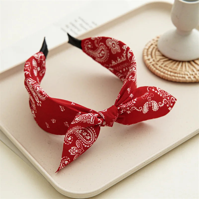 A red paisley bandana headband tied in a bow resting on a light surface.