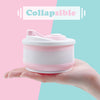 A hand holds a pink silicone collapsible coffee cup with a lid against a light pink and teal background.