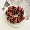 A brown satin scrunchie tied in a rosette shape resting on a white surface.