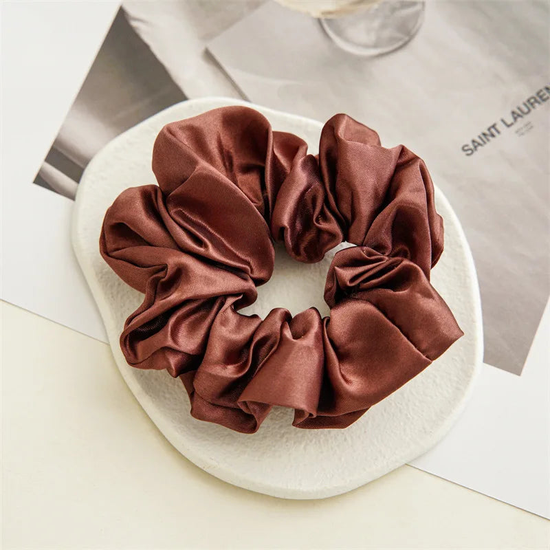 A brown satin scrunchie tied in a rosette shape resting on a white surface.