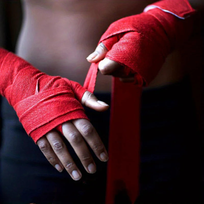 A close-up of a hand wrapped in red cotton boxing hand wraps being tied by another hand.